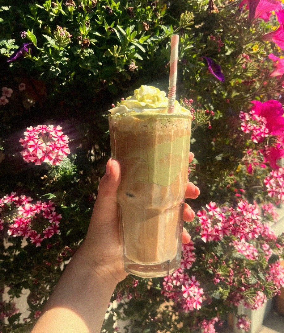 Hand holding a refreshing iced coffee drink from Mamma J's against a backdrop of colourful flowers