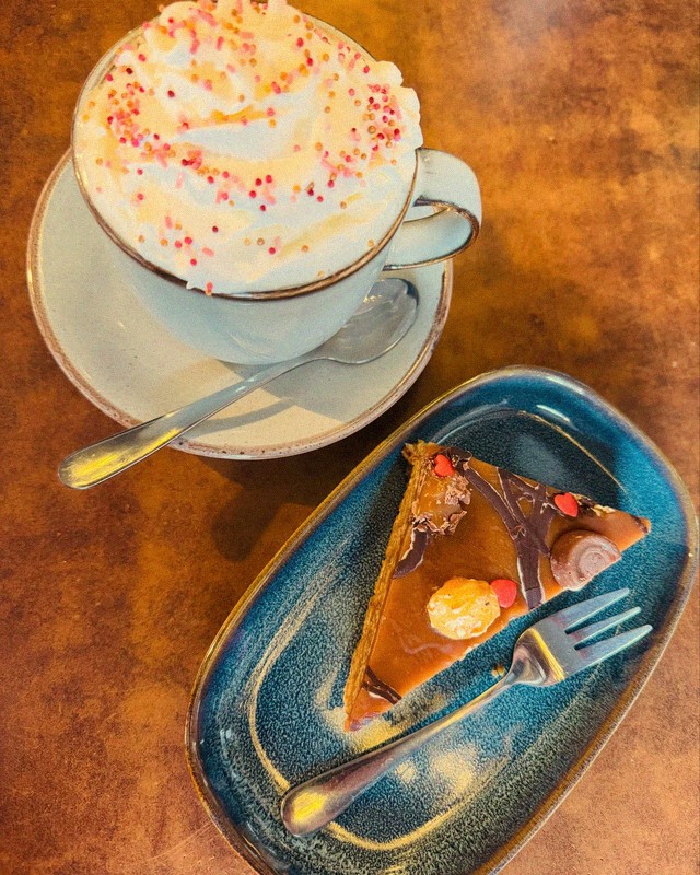 Creamy hot coffee with whipped cream and sprinkles alongside a caramel cake slice on a blue ceramic plate