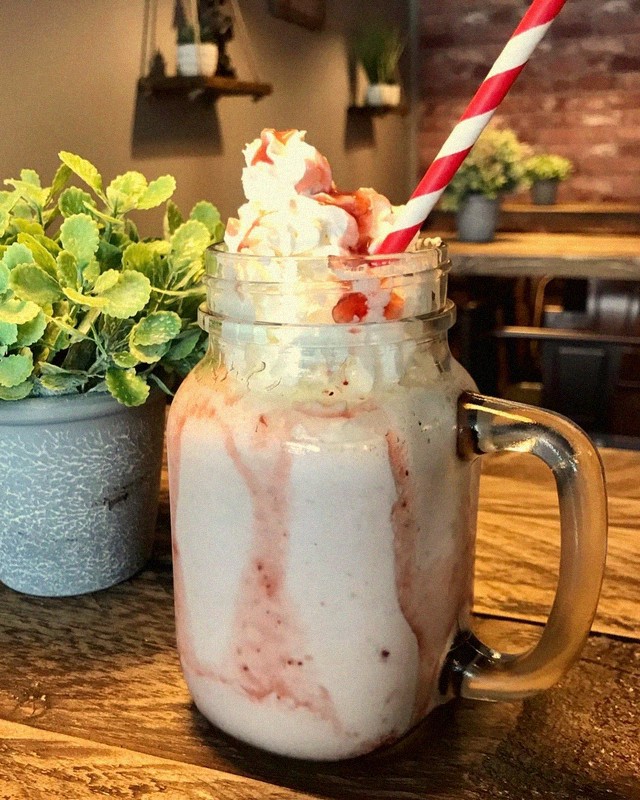 Strawberry milkshake topped with whipped cream and sprinkles served in a mason jar at Mamma J's
